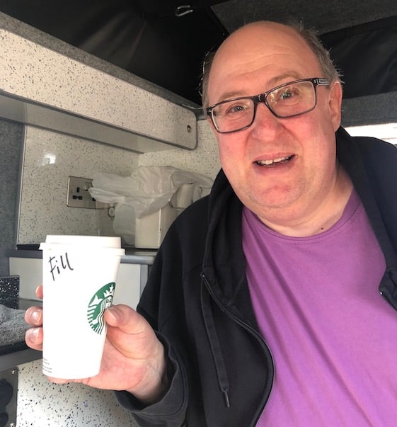 Phil from CooWooDoo in campervan holding Starbucks coffee with his name spelled Fill not Phil