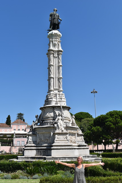 woman with outstretched arms in front of tall statue on column