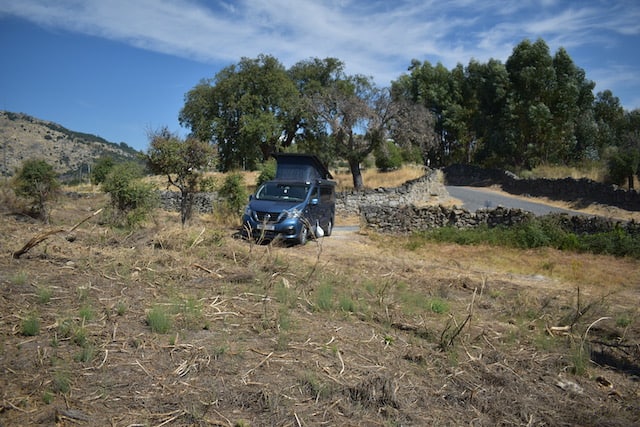 blue campervan parked on land in front of stone wall