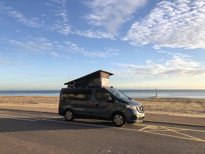 blue campervan parked on seafront with blue skies and some clouds overhead