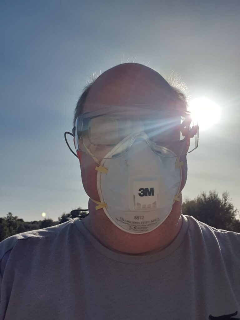 man outside in sunshine, wearing dust mask